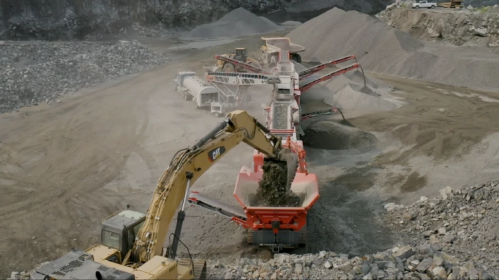 破碎机厂家正在作业的 200TPH 玄武岩砂石生产线实拍，CAT 挖掘机向移动破碎站给料。